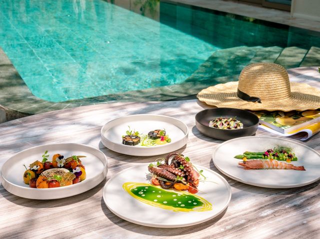 Four plates of food are sitting on a table next to a pool.