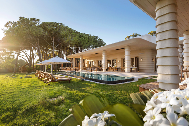 A large white house with a swimming pool in the backyard surrounded by trees.