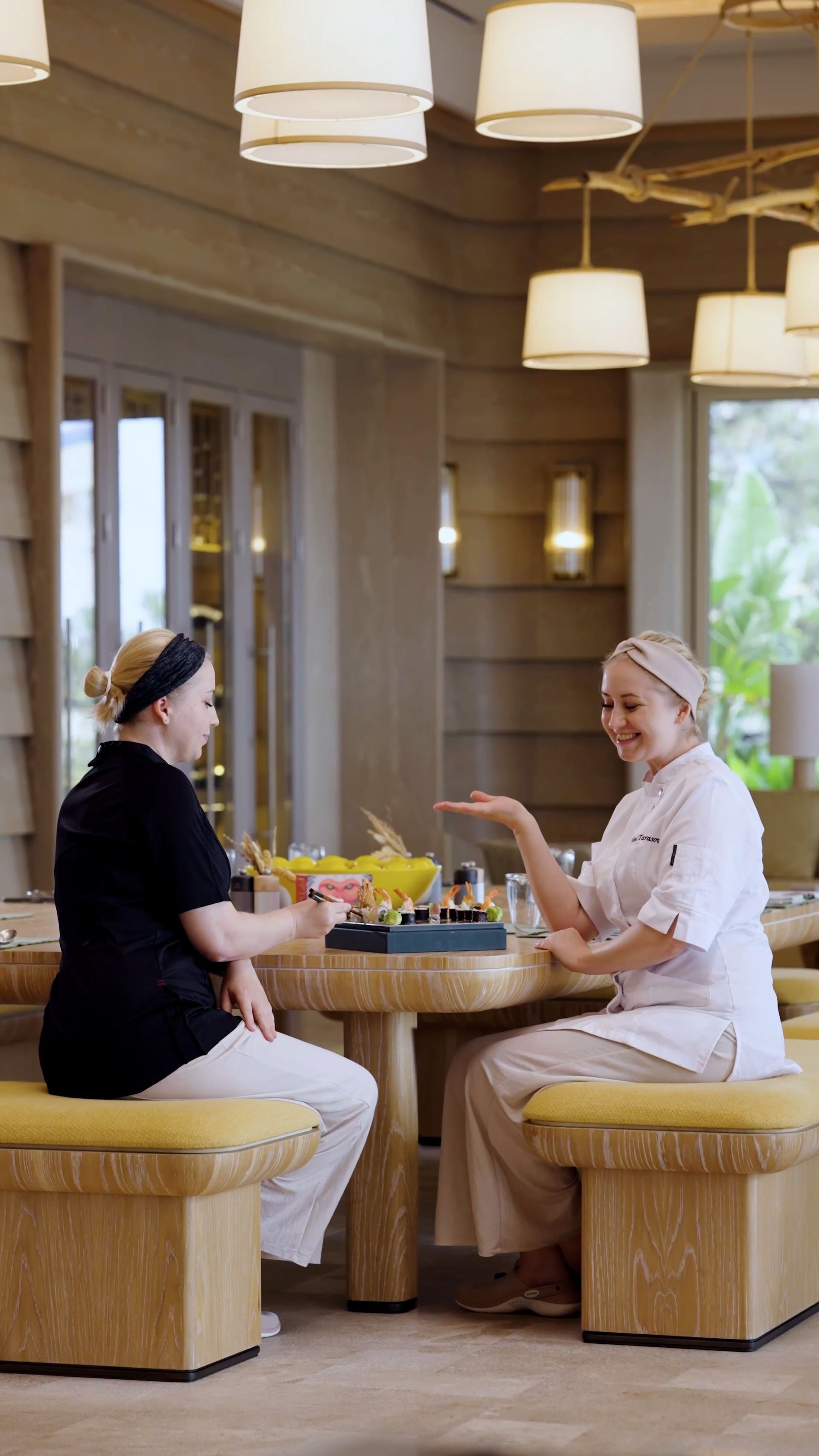 Two women are sitting at a table in a restaurant talking to each other.