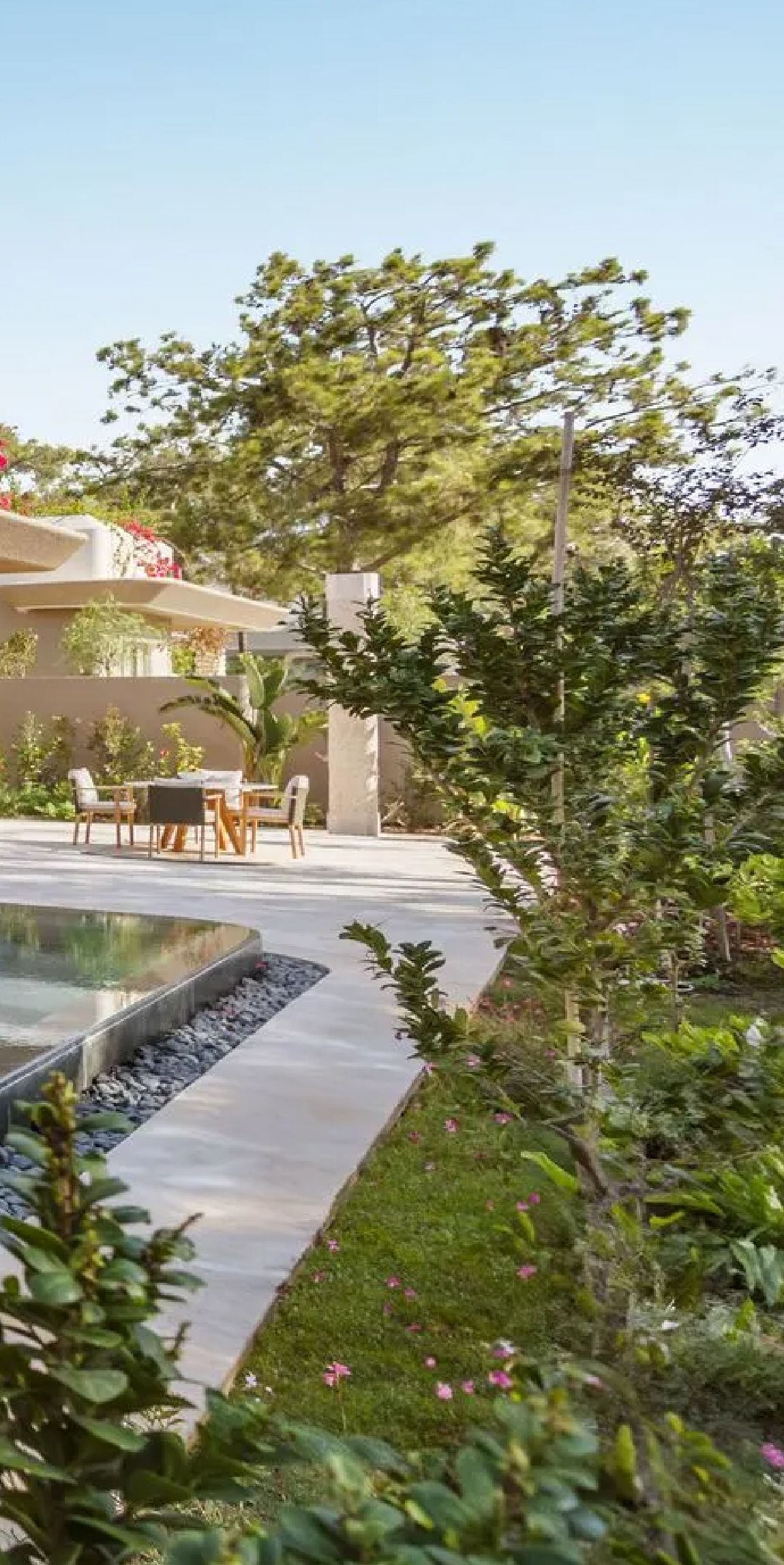 A patio with a table and chairs and a swimming pool surrounded by trees and bushes.