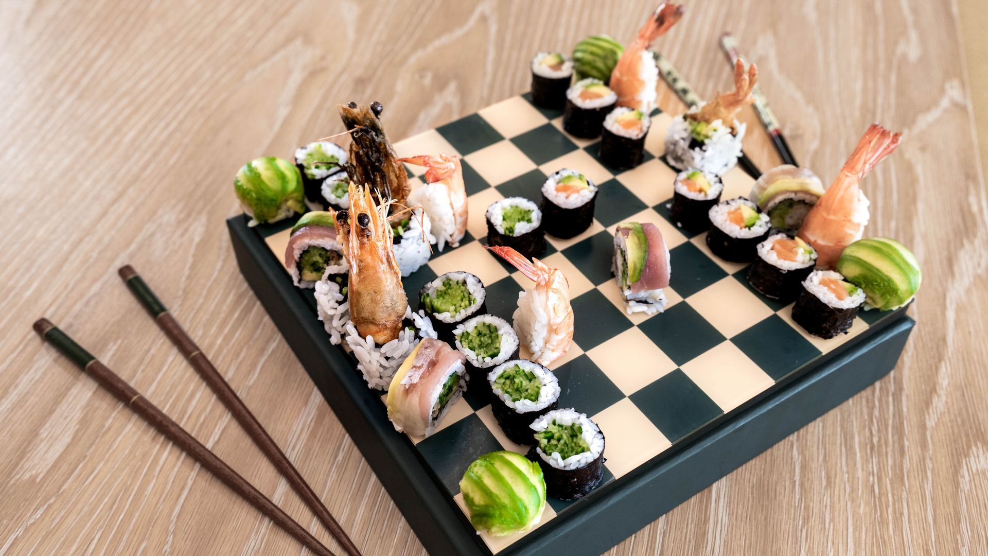 A chess board filled with sushi and chopsticks on a wooden table.